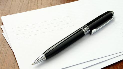 Schwarzer Kugelschreiber liegt auf einem Stapel weißer Blätter auf einer Holzoberfläche.